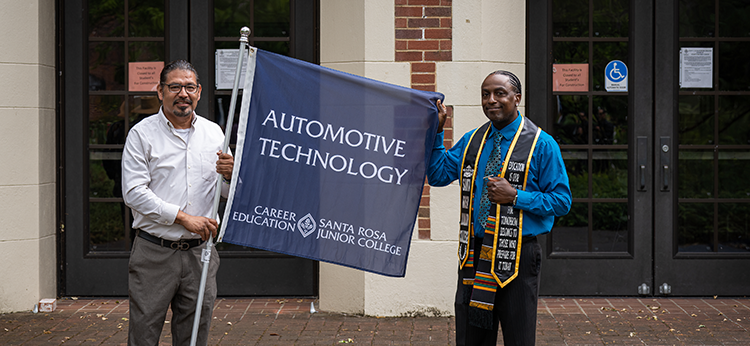 Two male adult students are holding a flag with the inscription Automotive Technology – Career Education, Santa Rosa Junior College. The photo illustrates the annual Celebrate CE event for students who achieved career and skills certificates. 